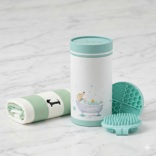 Kit de baño esencial premium para perros sobre superficie de mármol elegante. Incluye toalla absorbente a rayas, cepillo de masaje de silicona, alfombrilla lick mat y envase cilíndrico ilustrado.